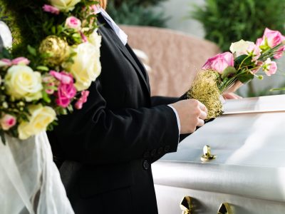 Mourning man and woman on funeral with pink rose standing at casket or coffin